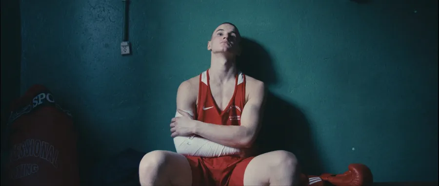 Łukasz Perkowski in a red boxing kit sitting against a wall
